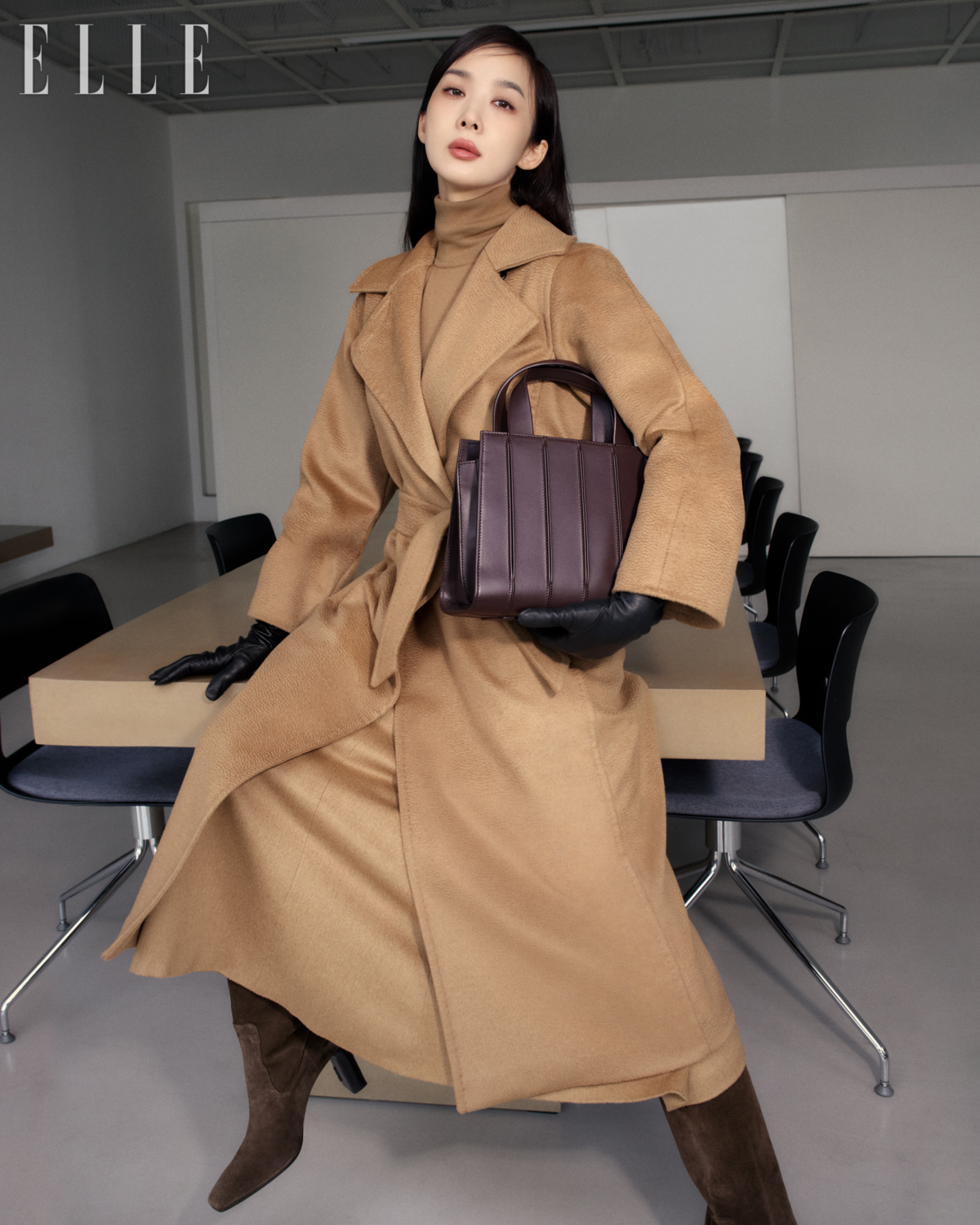 벨트 디테일의 마누엘라 아이콘 코트, 스웨터, A라인 실루엣의 스커트, 글러브, 휘트니 백, 슬라우치 레더 부츠는 Max Mara. 