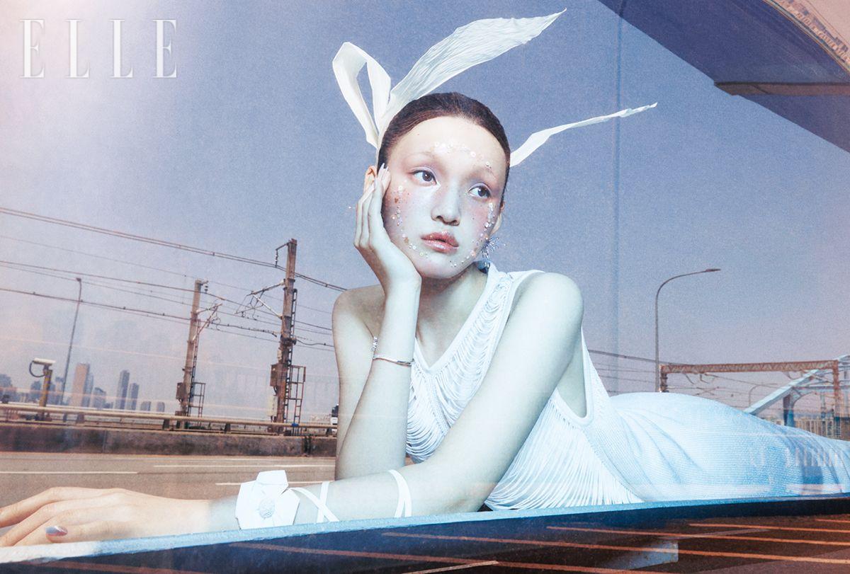 화이트 드레스는 Akris. 이어링은 Uselessobjects. 오른손의 브레이슬릿은 Swarovski. 왼손의 암 스트랩은 Ice Dust. 날개는 Kowgi.