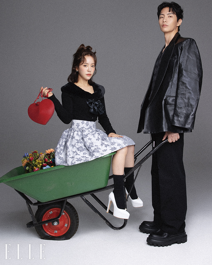  이민기가 입은 블랙 레더 재킷은 Valentino. 아가일 패턴의 베스트는 Polo by Ralph Lauren. 팬츠는 Marni by 10 Corso Como Seoul. 레이스업 슈즈는 Dolce & Gabbana. 한지민이 입은 보 카디건은 Weird Market. 러플 미니스커트는 Bmuet(te). 레드 백은 Alaïa. 귀고리는 Golden Dew. 화이트 스틸레토 힐은 Irostyle.