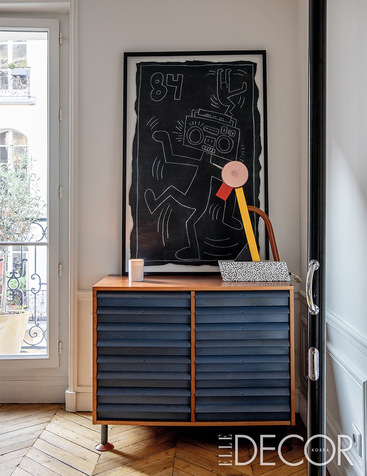 거실 한쪽에 놓인 빈티지 수납장 위에는 에토레 소트사스의 ‘타히티(Tahiti)’ 램프와 키스 해링의 드로잉이 놓여 있다. 손잡이가 달린 블랙 ‘칼리마코(Callimaco)’ 조명은 아르테미데.